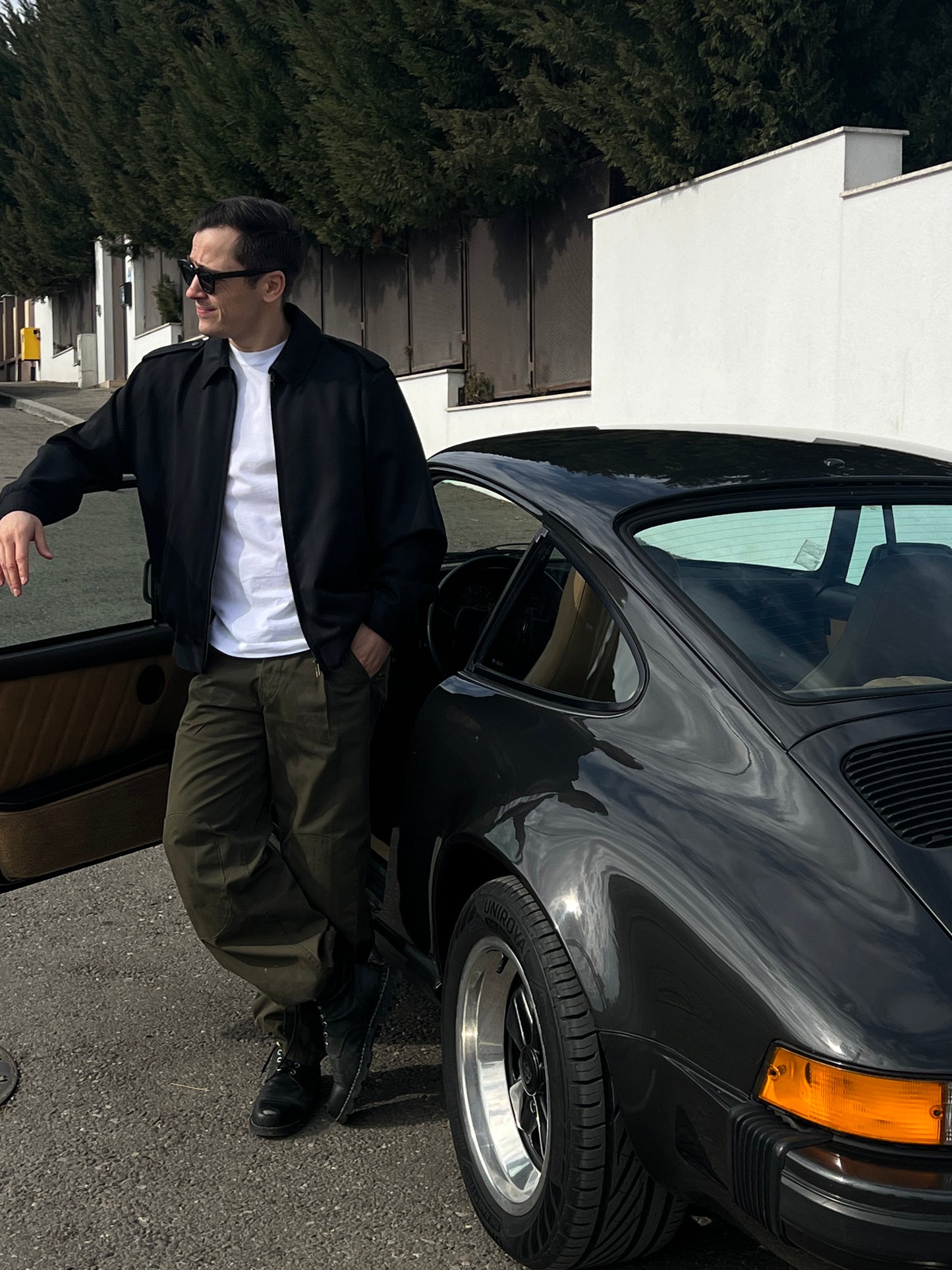 man standing next to a car wearing a black army wool jacket